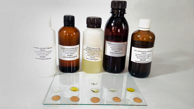 Porovnanie oljov pri tvorbe tekutého minerálneho make-upu. Sklenené fľaše stoja na bielom pozadí a na kúsku skla sú farebné olejové kvapky.